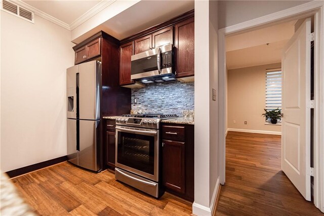 kitchen with backsplash, ornamental molding, stainless steel appliances, and light hardwood / wood-style floors