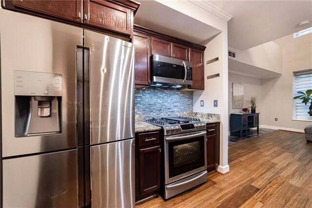 kitchen featuring light stone counters, backsplash, dark brown cabinets, appliances with stainless steel finishes, and light wood-type flooring