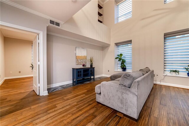 living room featuring plenty of natural light, dark hardwood / wood-style flooring, ornamental molding, and a high ceiling