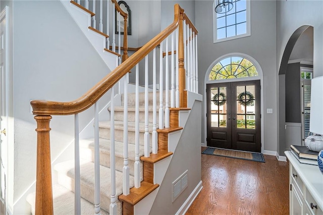 foyer entrance featuring a towering ceiling, french doors, and wood-type flooring