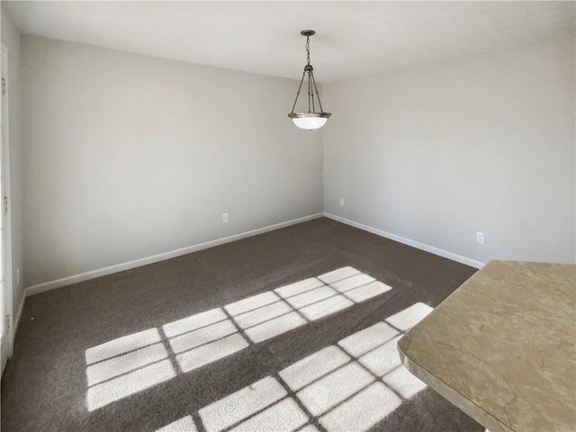 spare room featuring dark colored carpet and baseboards