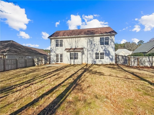 rear view of house featuring a fenced backyard, french doors, and a yard