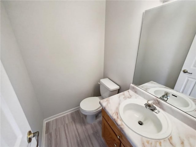 half bathroom featuring baseboards, vanity, toilet, and wood finished floors