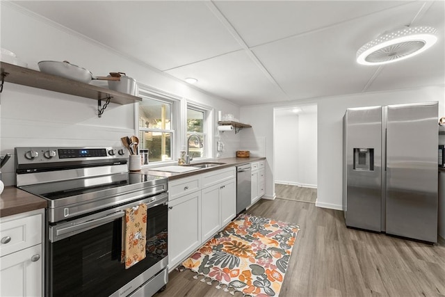 kitchen featuring open shelves, dark countertops, light wood-style flooring, appliances with stainless steel finishes, and a sink