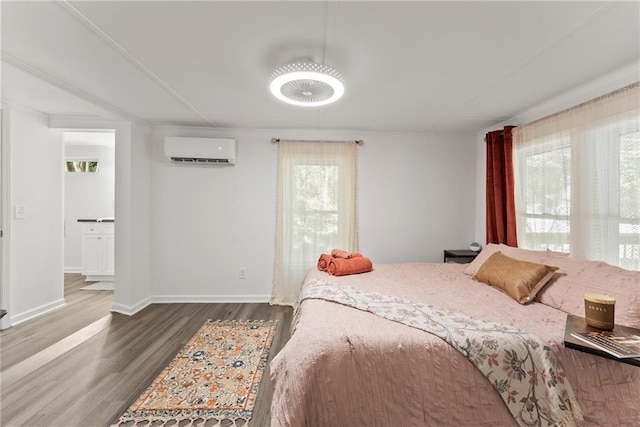 bedroom featuring a wall mounted AC, wood finished floors, and baseboards