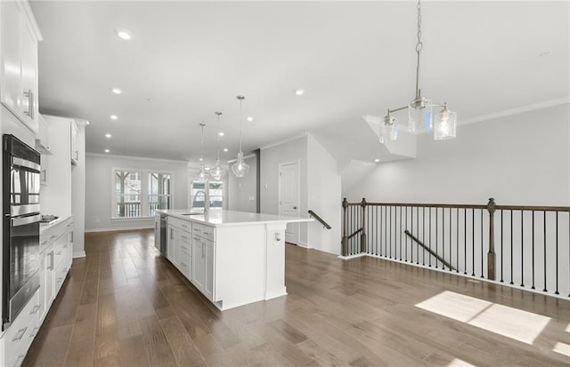 kitchen featuring dark wood-type flooring, decorative light fixtures, a center island with sink, white cabinets, and ornamental molding