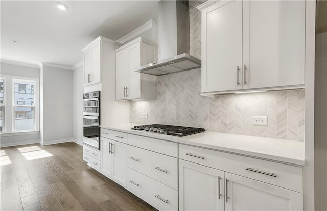 kitchen featuring wall chimney exhaust hood, dark hardwood / wood-style floors, ornamental molding, white cabinetry, and stainless steel appliances