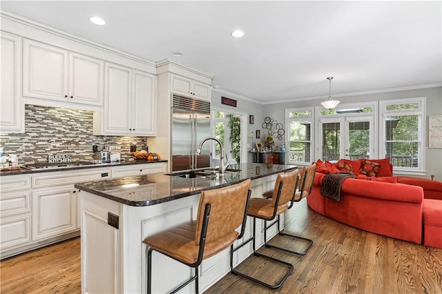 kitchen with hanging light fixtures, sink, light hardwood / wood-style flooring, an island with sink, and appliances with stainless steel finishes