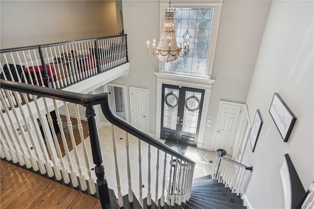 stairs featuring hardwood / wood-style flooring, a notable chandelier, a high ceiling, and french doors