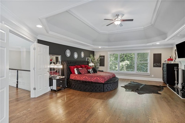 bedroom with hardwood / wood-style floors, a tray ceiling, ceiling fan, and crown molding