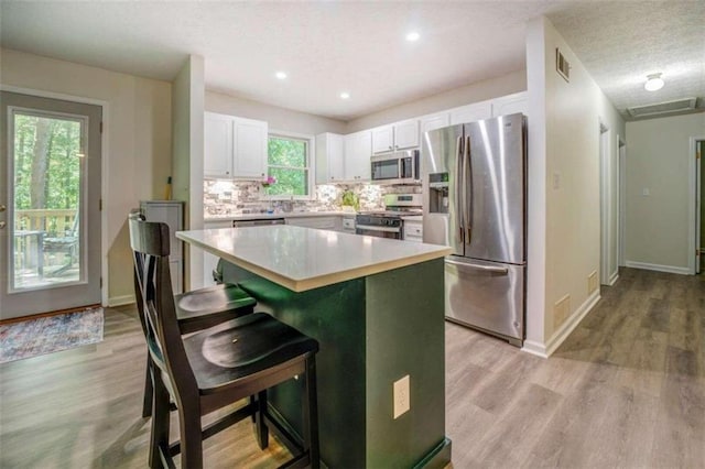 kitchen with a breakfast bar area, appliances with stainless steel finishes, white cabinets, and light hardwood / wood-style floors