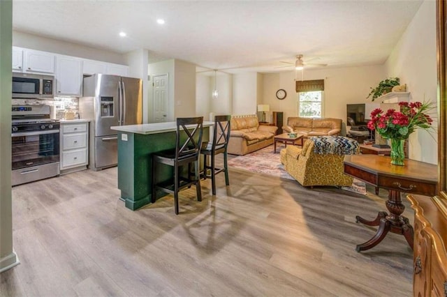 kitchen featuring light hardwood / wood-style floors, a breakfast bar, stainless steel appliances, ceiling fan, and white cabinets