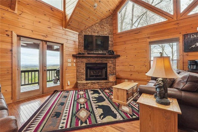 living room with wood-type flooring, a fireplace, wooden walls, and high vaulted ceiling