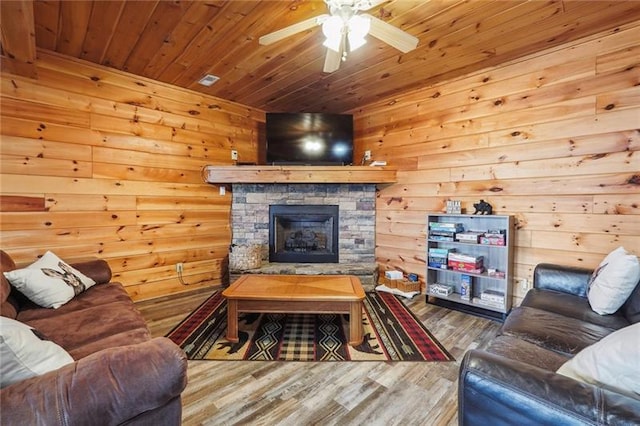 living room featuring wood walls, hardwood / wood-style floors, a stone fireplace, ceiling fan, and wooden ceiling