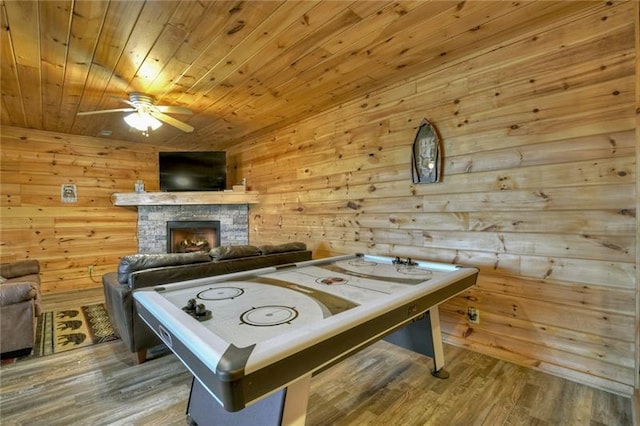 game room with wooden ceiling, a stone fireplace, wood walls, and hardwood / wood-style flooring