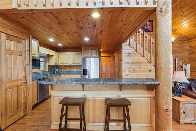 kitchen with appliances with stainless steel finishes, wooden walls, a breakfast bar area, and light hardwood / wood-style flooring