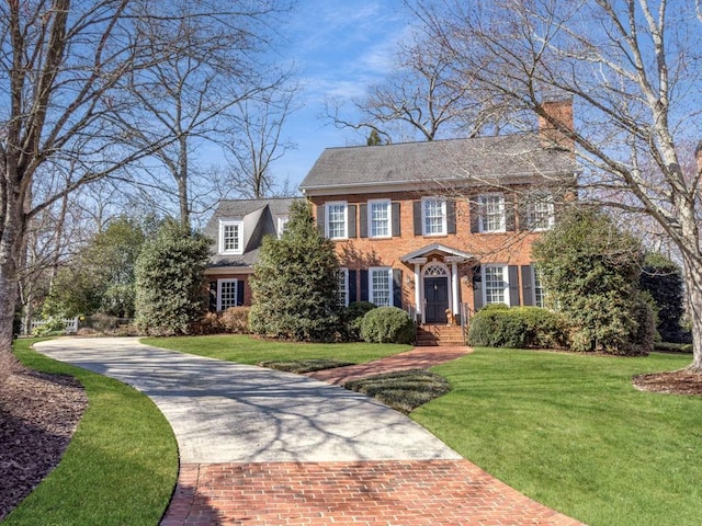 colonial house with brick siding, decorative driveway, and a front yard