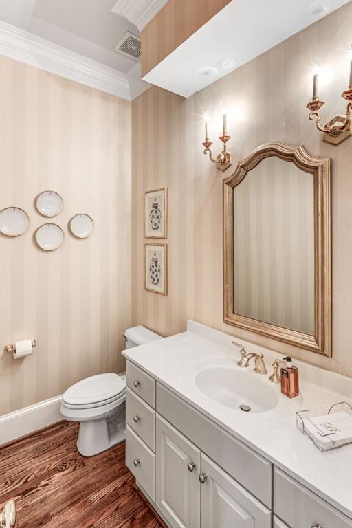 half bath featuring wood finished floors, crown molding, toilet, and wallpapered walls