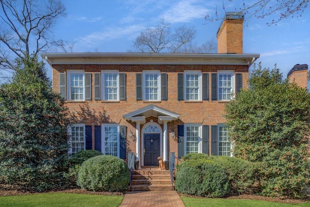 view of front facade with a chimney and brick siding