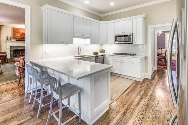 kitchen featuring light wood finished floors, appliances with stainless steel finishes, white cabinets, a sink, and a peninsula