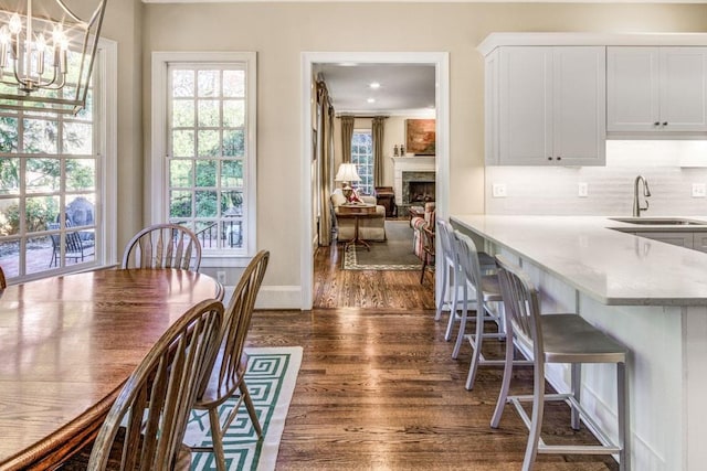 dining room featuring dark wood-style floors, a fireplace, baseboards, and an inviting chandelier