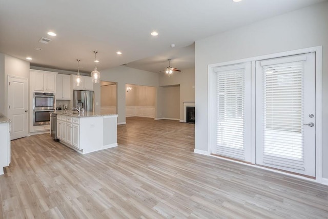 kitchen featuring white cabinetry, a center island with sink, stainless steel appliances, ceiling fan, and pendant lighting