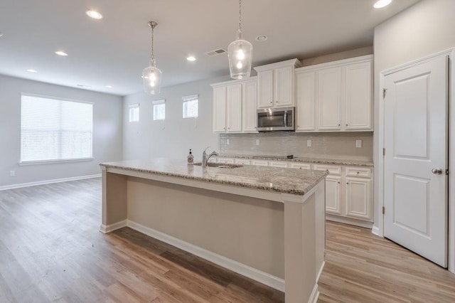 kitchen with backsplash, white cabinets, a kitchen island with sink, and pendant lighting