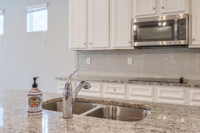 kitchen with white cabinetry, sink, backsplash, light stone counters, and black electric stovetop