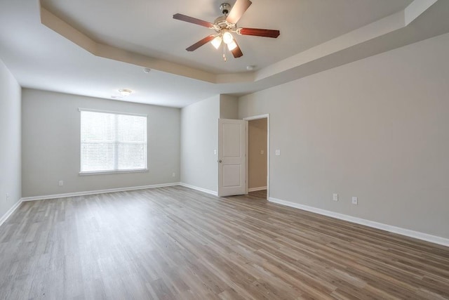 empty room featuring ceiling fan, a raised ceiling, and wood-type flooring