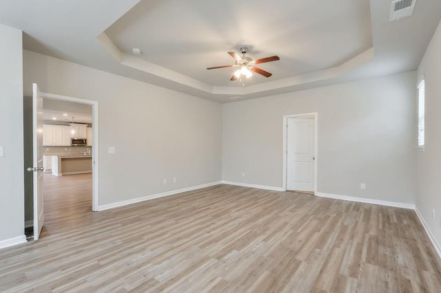 unfurnished room featuring light wood-type flooring, ceiling fan, and a raised ceiling