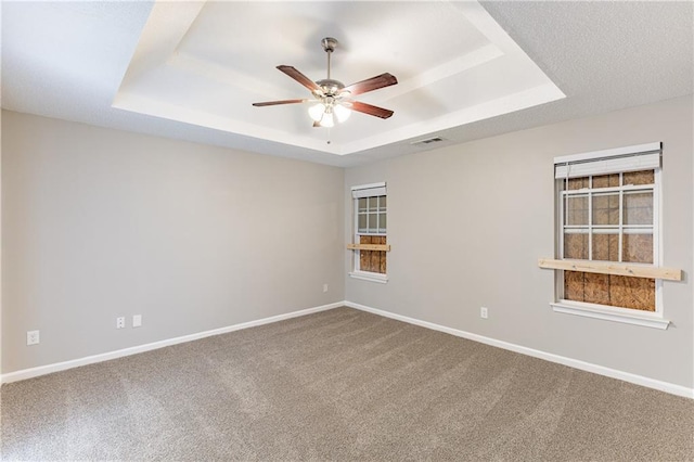 unfurnished room with carpet floors, visible vents, a tray ceiling, and baseboards