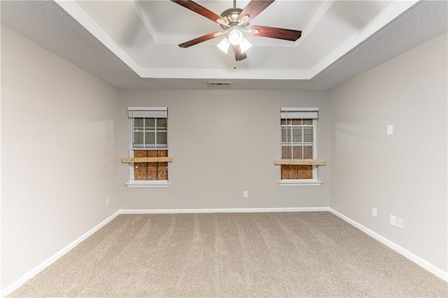 carpeted spare room with a textured ceiling, a ceiling fan, visible vents, baseboards, and a raised ceiling