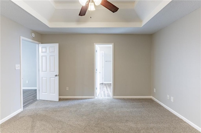 carpeted empty room featuring a tray ceiling, a ceiling fan, and baseboards