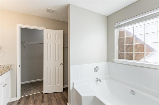 full bath with a garden tub, wood finished floors, visible vents, vanity, and a spacious closet