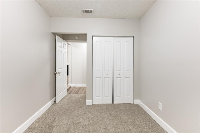 unfurnished bedroom featuring baseboards, visible vents, a textured ceiling, carpet floors, and a closet