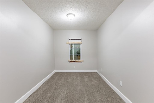 empty room featuring a textured ceiling, dark colored carpet, and baseboards