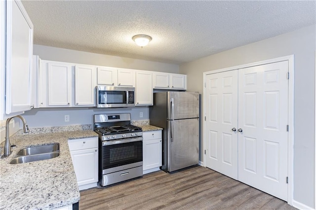 kitchen with white cabinets, light wood finished floors, stainless steel appliances, and a sink