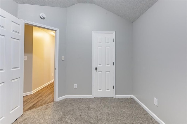 carpeted empty room with baseboards, vaulted ceiling, and a textured ceiling