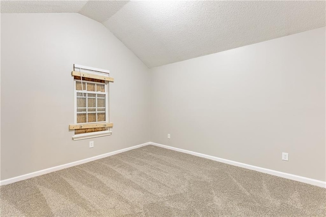 spare room with vaulted ceiling, a textured ceiling, carpet, and baseboards