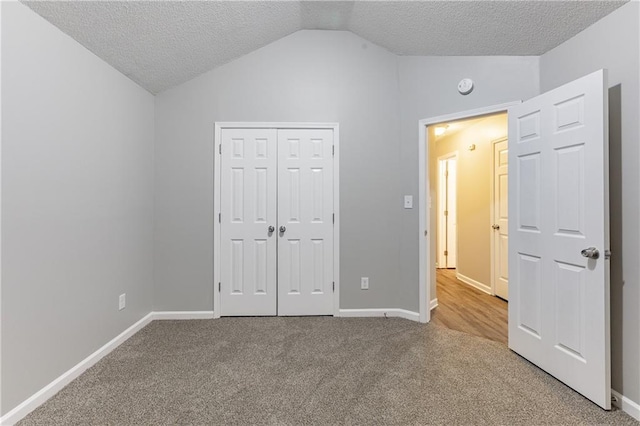 unfurnished bedroom featuring lofted ceiling, baseboards, a textured ceiling, and carpet