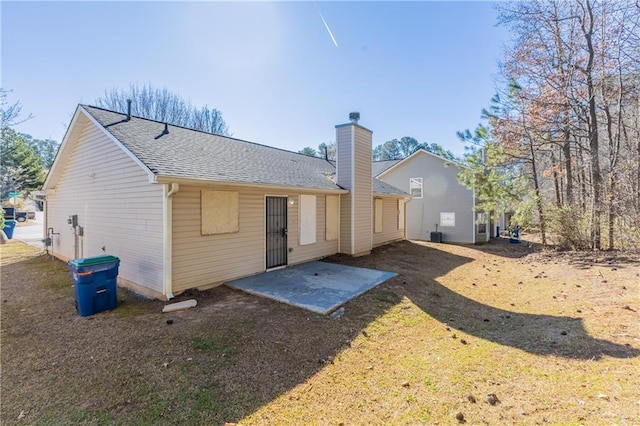 rear view of house featuring a patio, a shingled roof, and a chimney