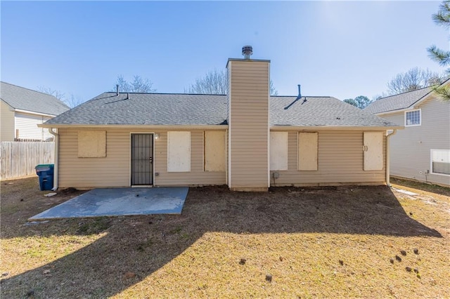 back of house featuring a shingled roof, a lawn, a chimney, fence, and a patio area