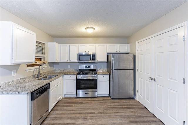 kitchen featuring appliances with stainless steel finishes, dark wood-type flooring, white cabinetry, a sink, and light stone countertops