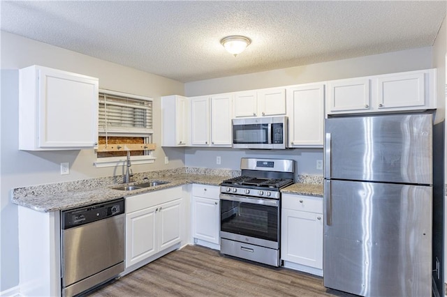 kitchen with stainless steel appliances, white cabinetry, and light wood-style floors