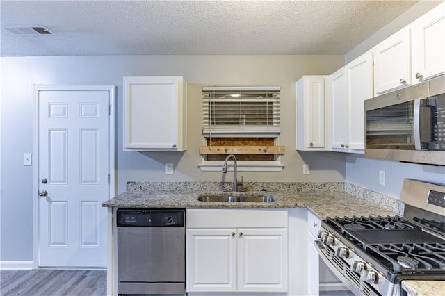 kitchen with visible vents, white cabinets, light stone countertops, stainless steel appliances, and a sink