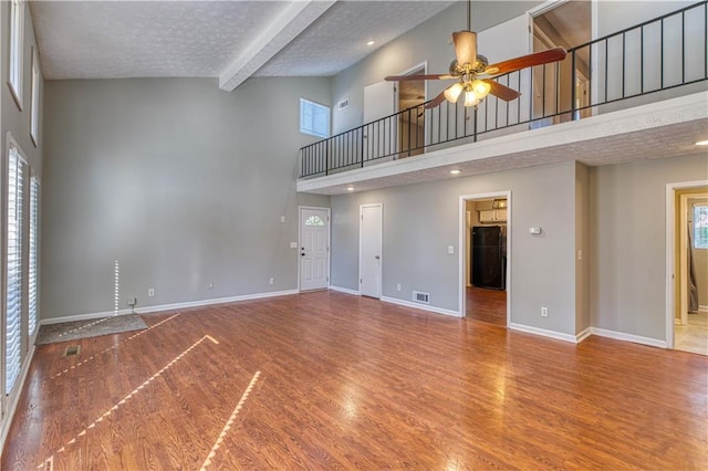 unfurnished living room with beam ceiling, ceiling fan, and a towering ceiling