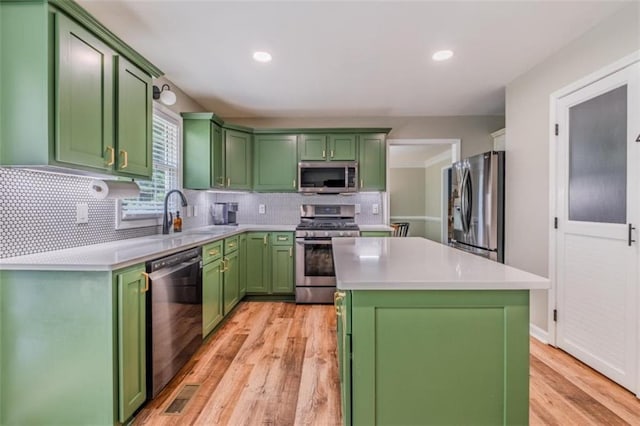 kitchen with a sink, stainless steel appliances, light wood-style flooring, light countertops, and green cabinets
