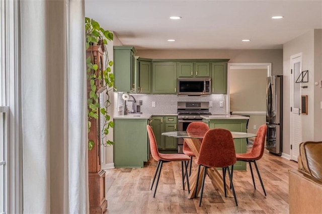kitchen with recessed lighting, green cabinets, decorative backsplash, light wood-style floors, and stainless steel appliances