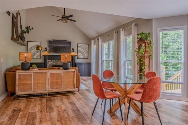 dining room featuring light wood-style floors, lofted ceiling, a ceiling fan, and a stone fireplace