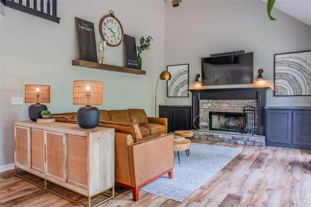 living room featuring wood finished floors, a stone fireplace, and high vaulted ceiling